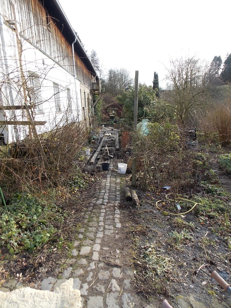 Hier sieht man die Neugestaltung des Pflasterweges. Die vorher in Längsrichtung ausgerichtete Pflasterung  wird nun im 90° Winkel zu Laufrichtung umgestaltet. Im Hintergrund der Ziegelsteinbogen .